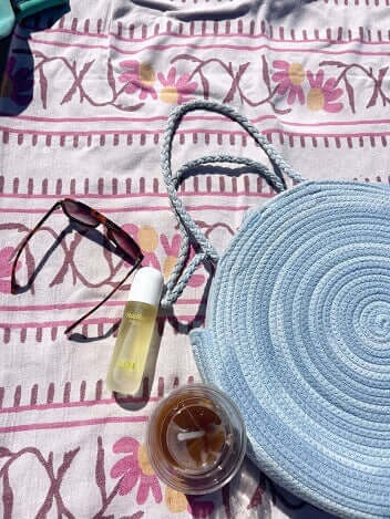 Blue woven bag, sunglasses, bottle, and jar on a patterned fabric background